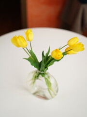 Bouquet of yellow tulips in a transparent glass vase stand on a white table