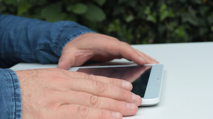 close-up hands of a man using his tablet on the table in the garden at home on daytime