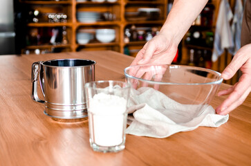 Hand pouring wholewheat flour into glass bowl on wooden table