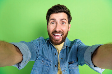 Photo of excited positive guy dressed jeans shirt tacking selfie empty space isolated green color...