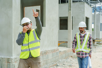 Construction site scene, male in high-visibility vest talks on phone, gesturing, another male looks...