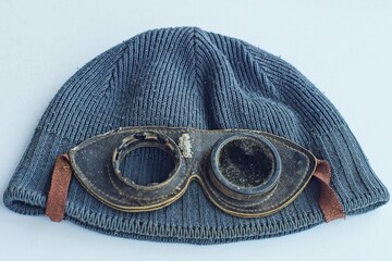 some old black leather frame broken round retro flight glass glasses lie on a gray men's cap on a white table