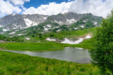 Lake in the Alpine mountains. Beautiful landscape with mountains, green grassy meadows and a hiking trail in springtime.
