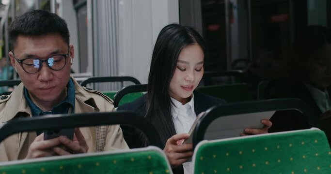 Side view of Asian people traveling together in train or bus. Taking public transport in night. Evening outside. People busy using their personal digital devices. Concept of passengers.