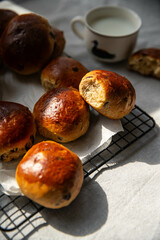 Freshly baked aromatic homemade chocolate and lemon brioche buns on cooling rack and cup of milk on linen tablecloth.
