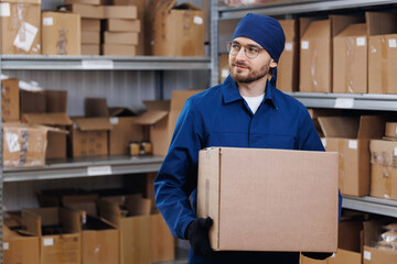 Worker in blue uniform hold cardboard box on background warehouse storage. Concept banner logistic...