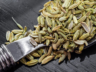Whole fennel seeds piled on a silver spoon dark wooden background
