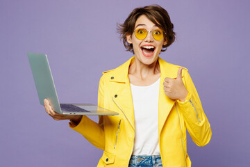 Young smiling IT woman wearing yellow shirt white t-shirt casual clothes glasses hold use work on laptop pc computer show thumb up isolated on plain pastel light purple background. Lifestyle concept.