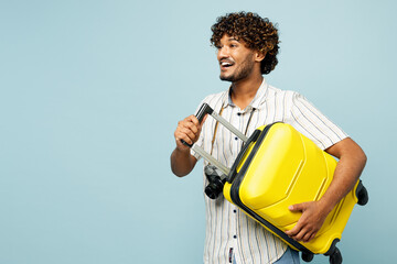 Side view traveler fun smiling Indian man wear white casual clothes hold bag isolated on plain blue background. Tourist travel abroad in free spare time rest getaway. Air flight trip journey concept.