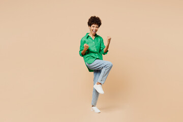 Fototapeta na wymiar Full body young woman of African American ethnicity wear green shirt casual clothes doing winner gesture celebrate clenching fists isolated on plain pastel light beige background. Lifestyle concept.