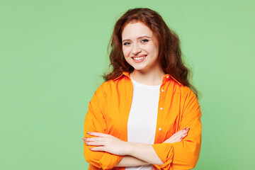 Fototapeta premium Young smiling happy cheerful ginger woman she wearing orange shirt white t-shirt casual clothes hold hands crossed folded look camera isolated on plain pastel light green background Lifestyle concept