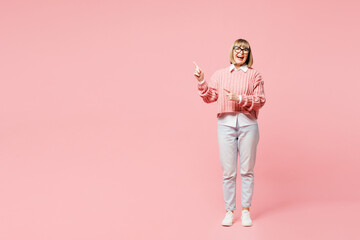 Full body elderly happy woman 50s years old wear sweater shirt casual clothes glasses point index finger aside on area isolated on plain pastel light pink background studio portrait Lifestyle concept