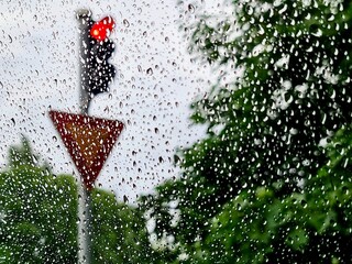 Rainy Day Mood: Water droplets on glass offer a distorted view of a traffic light and a yield sign,...