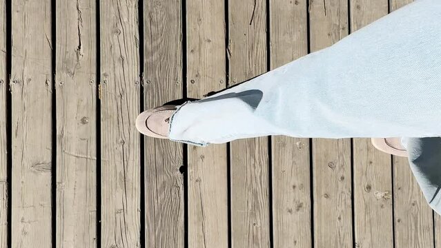 Female legs in moccasins and jeans walking along a wooden path, top view.