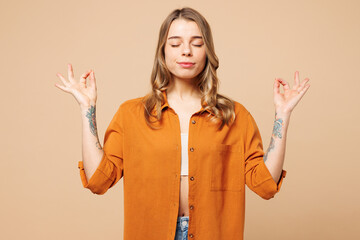 Young woman she wear orange shirt casual clothes hold spreading hands in yoga om aum gesture relax meditate try to calm down isolated on plain pastel light beige background studio. Lifestyle concept.