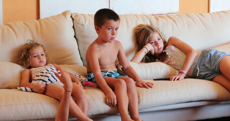 Kids at home seated on living room sofa children staring at TV screen watching movie