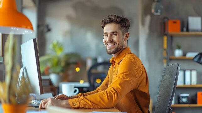 Young hipster man in sitting at the table and using laptop in the background of bright orange office