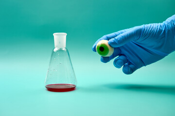 Conical flask with red substance and hand holding artificial eyeball