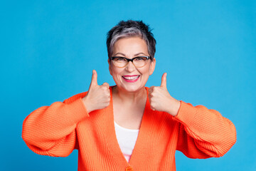 Photo of aged lady demonstrate thumb up wear orange cardigan isolated on blue color background