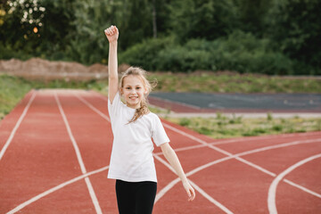 Fototapeta premium Cheerful pre-teen girl raises her hand up in victory on the running track. Sport and life accomplishment, teamwork, ,success concept