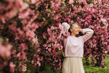 Young stylish woman wearing glasses surrounded by pink spring blossoms.