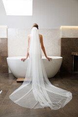 Woman in wedding robe and bridal veil sitting on the bathtub