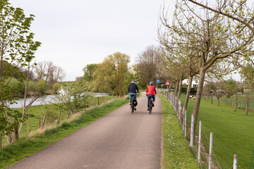 People cycle on the dike along the meadows and the Linge river.