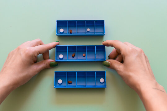 Organizing Medication with Weekly Pill Boxes on Green Background.