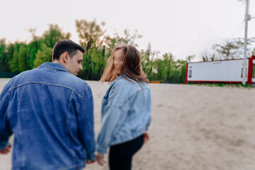 beautiful and young lovers, guy and girl kissing and hugging. Happy couple of European appearance on a first date outdoors on a beach with sand, smiling and relaxing