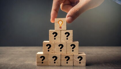 Hand put the last wooden cubes on the top of a pyramid built by wood toy with idea symbol, and many question marks at the base, got idea from many questions