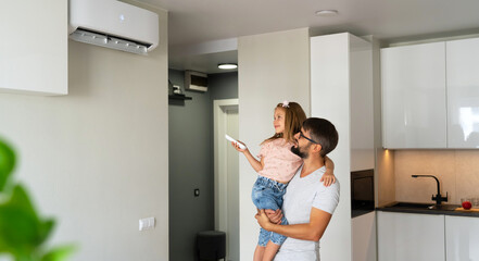 Father and little girl turn on air conditioner using remote control. Happy family adjust...