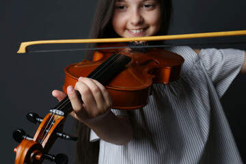 Preteen girl playing violin on black background, closeup