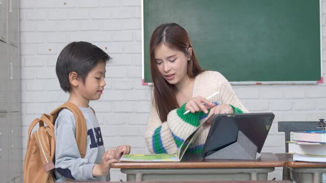 Smiling Asian female lecturer helping children student during classroom. Education knowledge, successful teamwork concept.