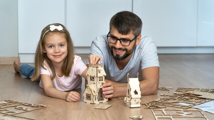 Happy father and child look at camera and laugh building wooden construction set. Family play with...