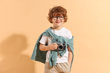 Fashion concept. Stylish boy with vintage camera on pale orange background
