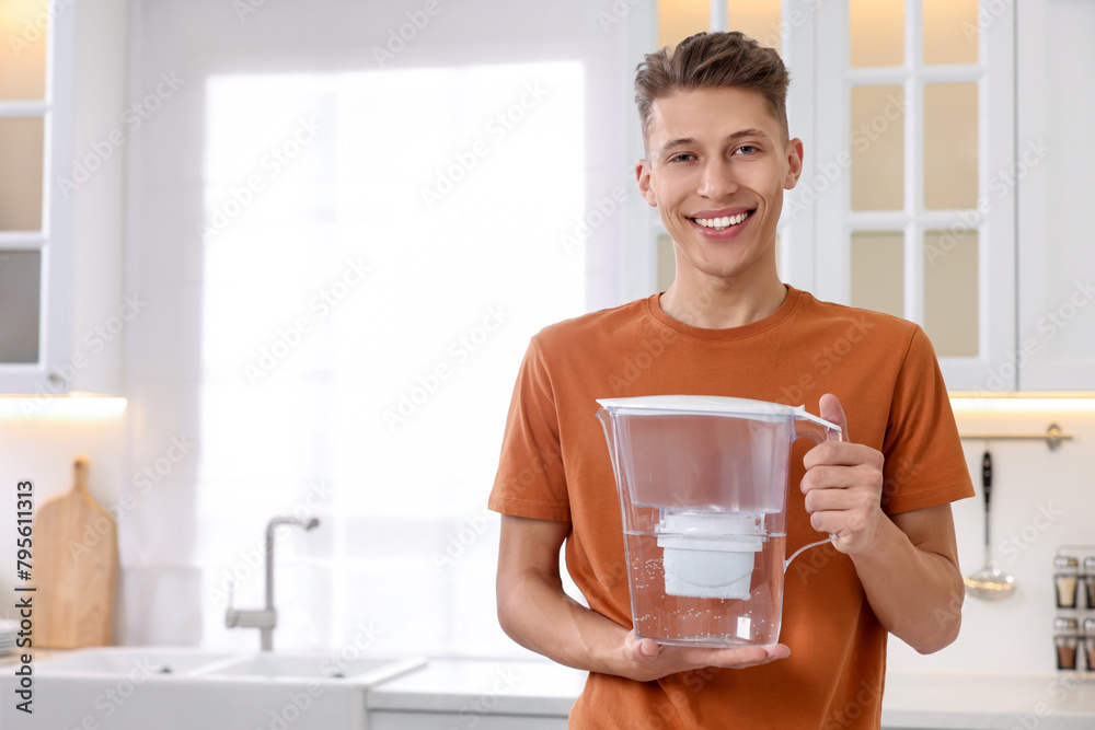 Poster Happy man with water filter jug in kitchen. Space for text