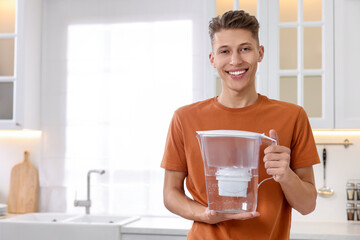 Happy man with water filter jug in kitchen. Space for text