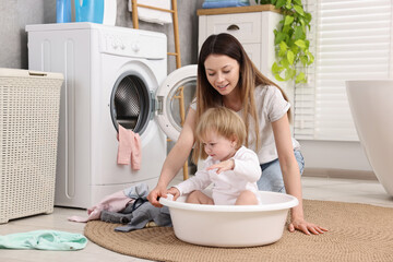 Happy mother with her daughter having fun while washing baby clothes in bathroom