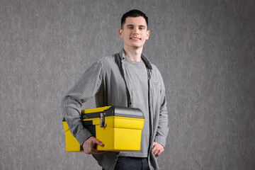 Young man with tool box on grey background
