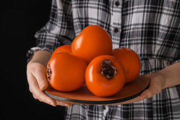 Woman holding delicious ripe juicy persimmons on black background, closeup