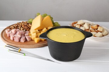 Fondue with tasty melted cheese, forks and different products on white wooden table