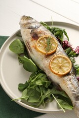 Baked fish with spinach and lemon on white wooden table, closeup