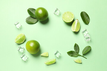 Frame made of ripe limes with leaves and ice cubes on light green background, flat lay