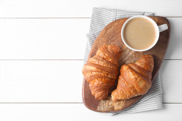 Tasty breakfast. Cup of coffee and croissants on white wooden table, top view. Space for text