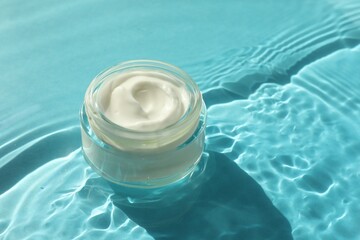 Jar with moisturizing cream in water on light blue background