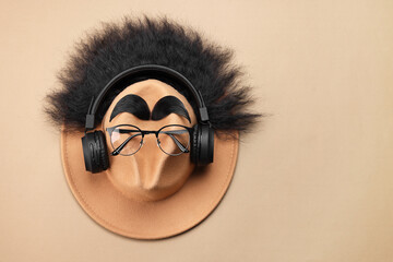 Man's face made of artificial hair, eyebrows, glasses and hat on beige background, top view. Space...