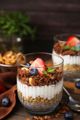 Tasty granola with berries, nuts, yogurt and chia seeds in glass on table