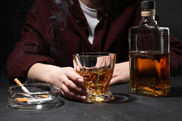 Alcohol addiction. Woman with whiskey and smoldering cigarettes at dark textured table, closeup