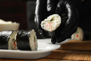 Chef in gloves putting sushi roll onto dish at table, closeup