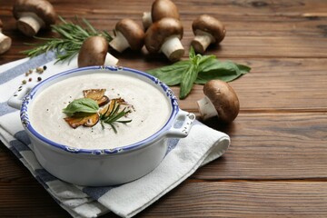 Delicious homemade mushroom soup in ceramic pot and fresh ingredients on wooden table. Space for text